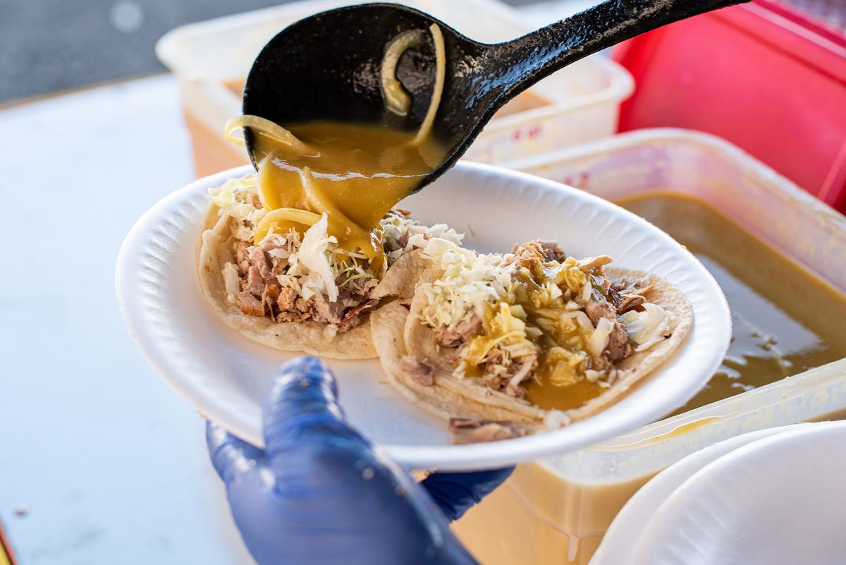 A ladle pours over yellow salsa onto pork tacos.