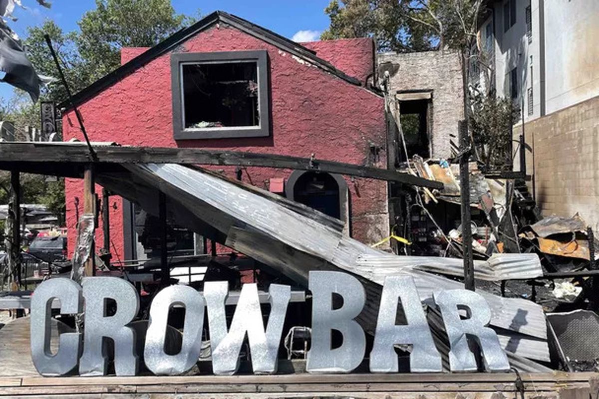 A damaged red building with large letters sitting in front reading Crow Bar.