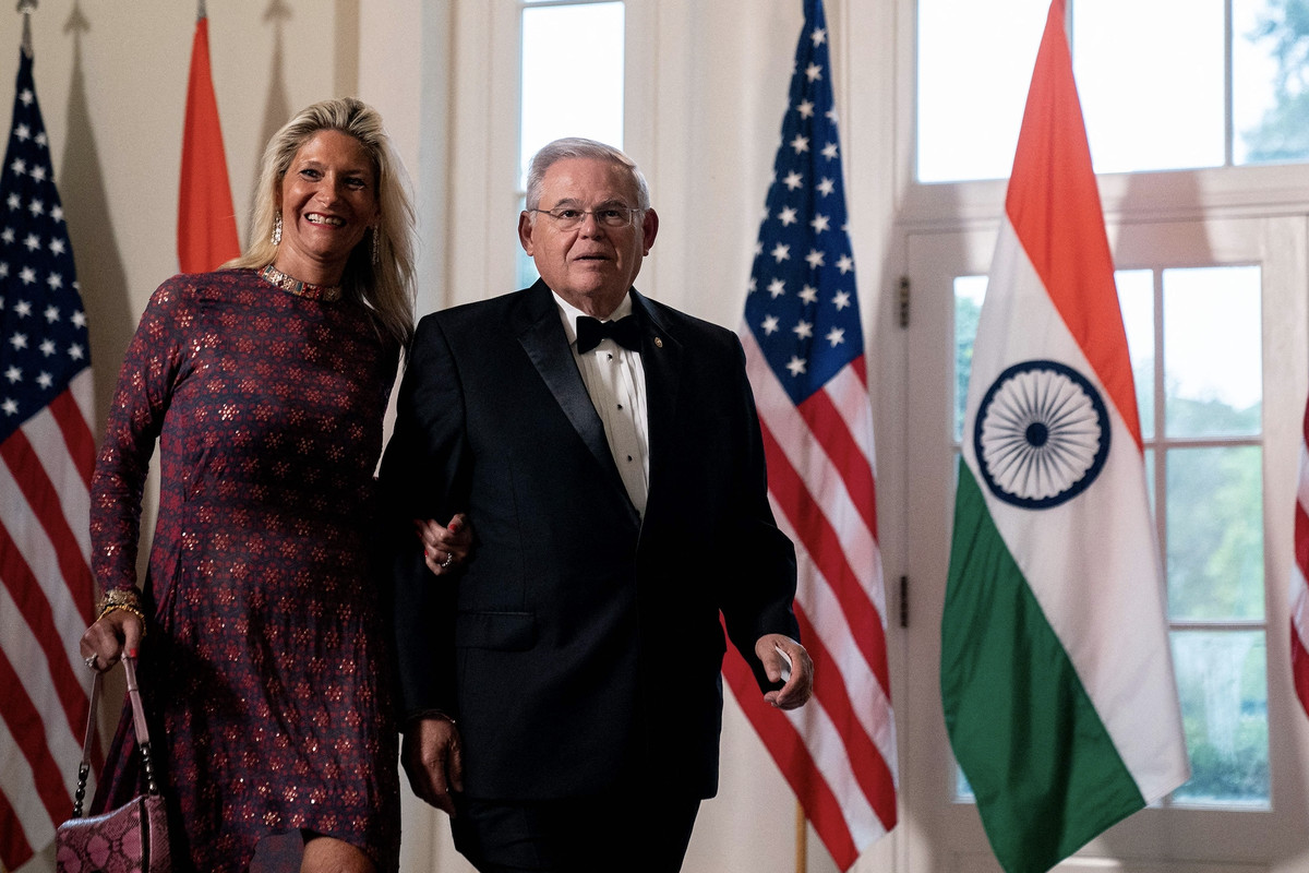 US Senator Bob Menendez and his wife stand inside the White House in front of a row of US and India flags.
