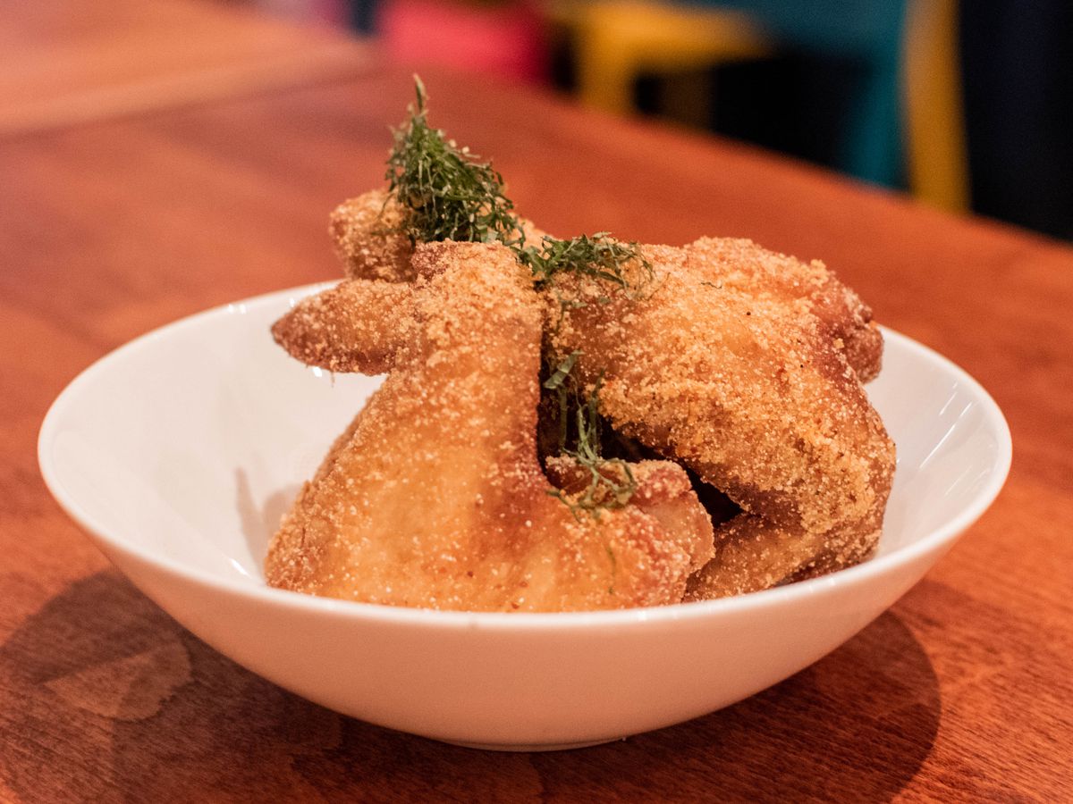 Several pieces of golden fried chicken wings with a green garnish sit in a white bowl.