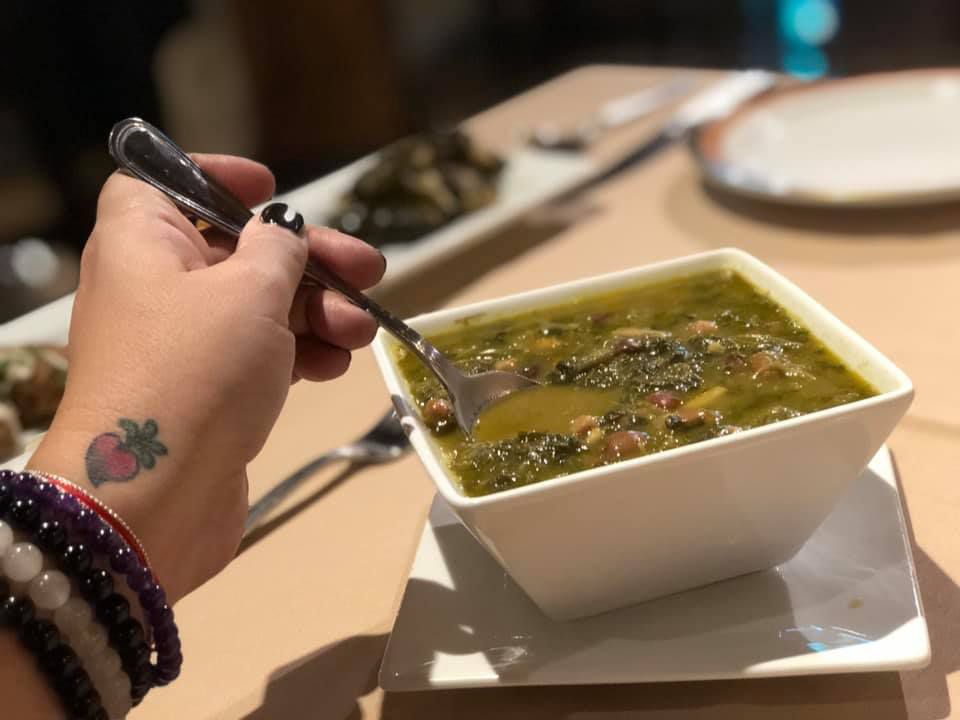 Bowl of green soup with spoon and hand