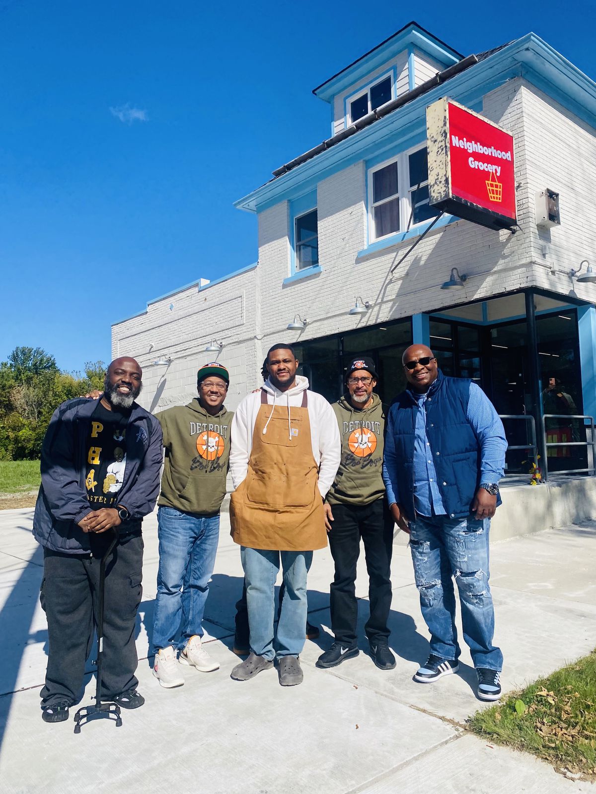 Four supporters standing around Raphael Wright, center, wearing a tan apron, standing outside of Neighborhood Grocery in Jefferson Chalmers in Detroit, Michigan.