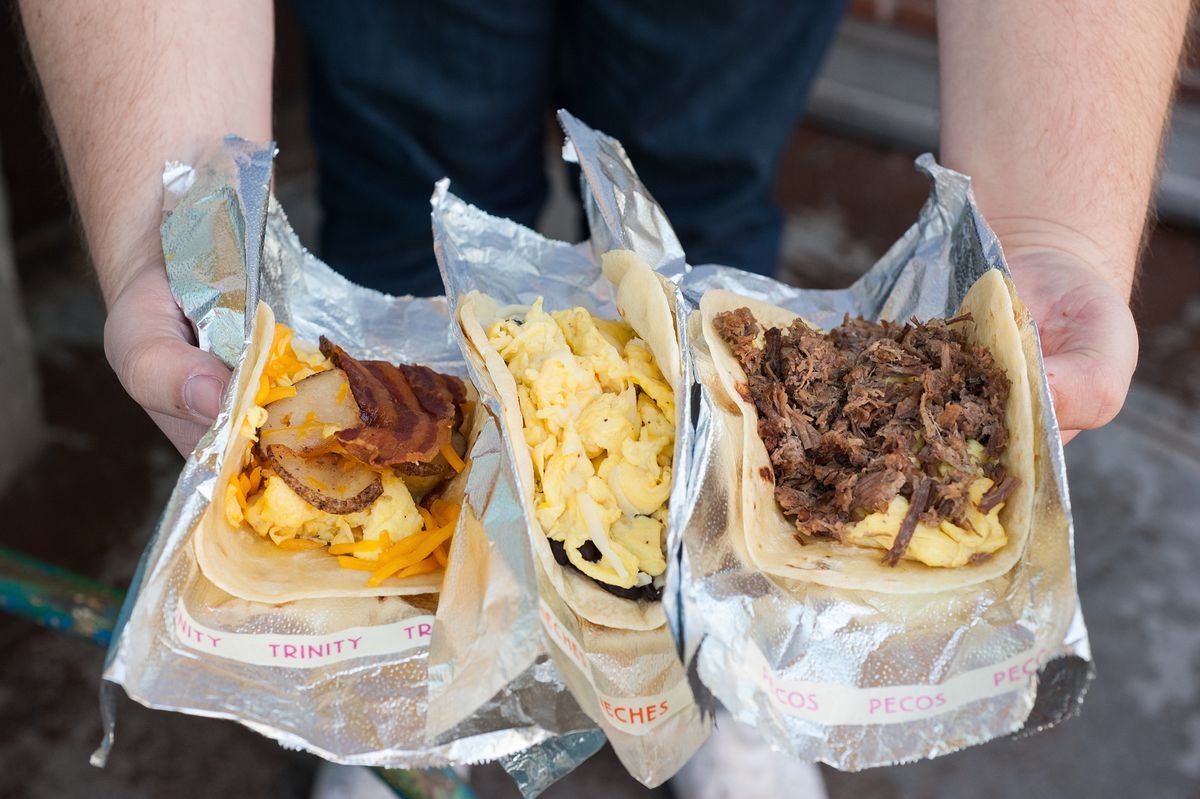 A person holds three different breakfast tacos from HomeState, wrapped in tin foil.