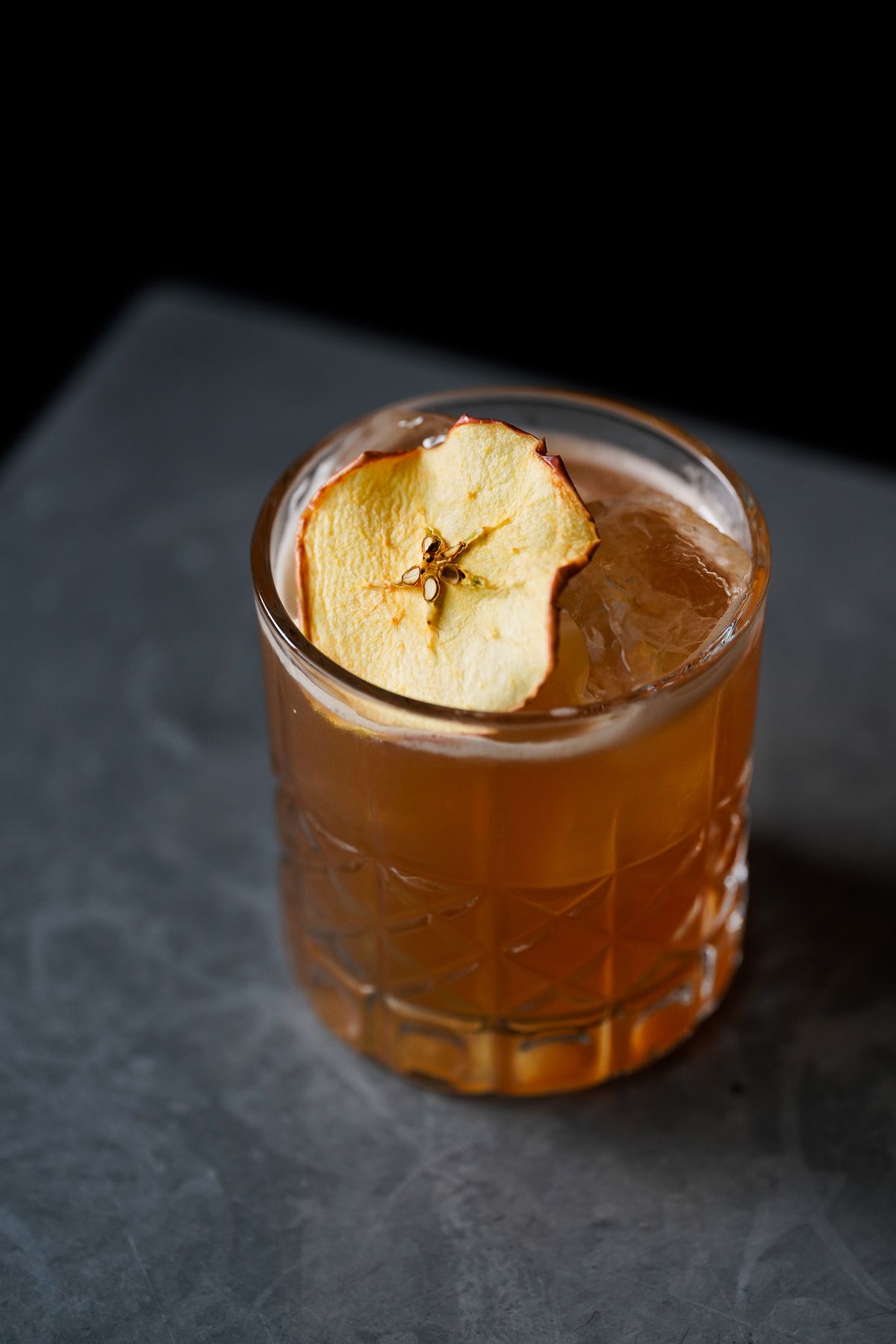 A light brown cocktail in a clear glass with a slice of dried pear.
