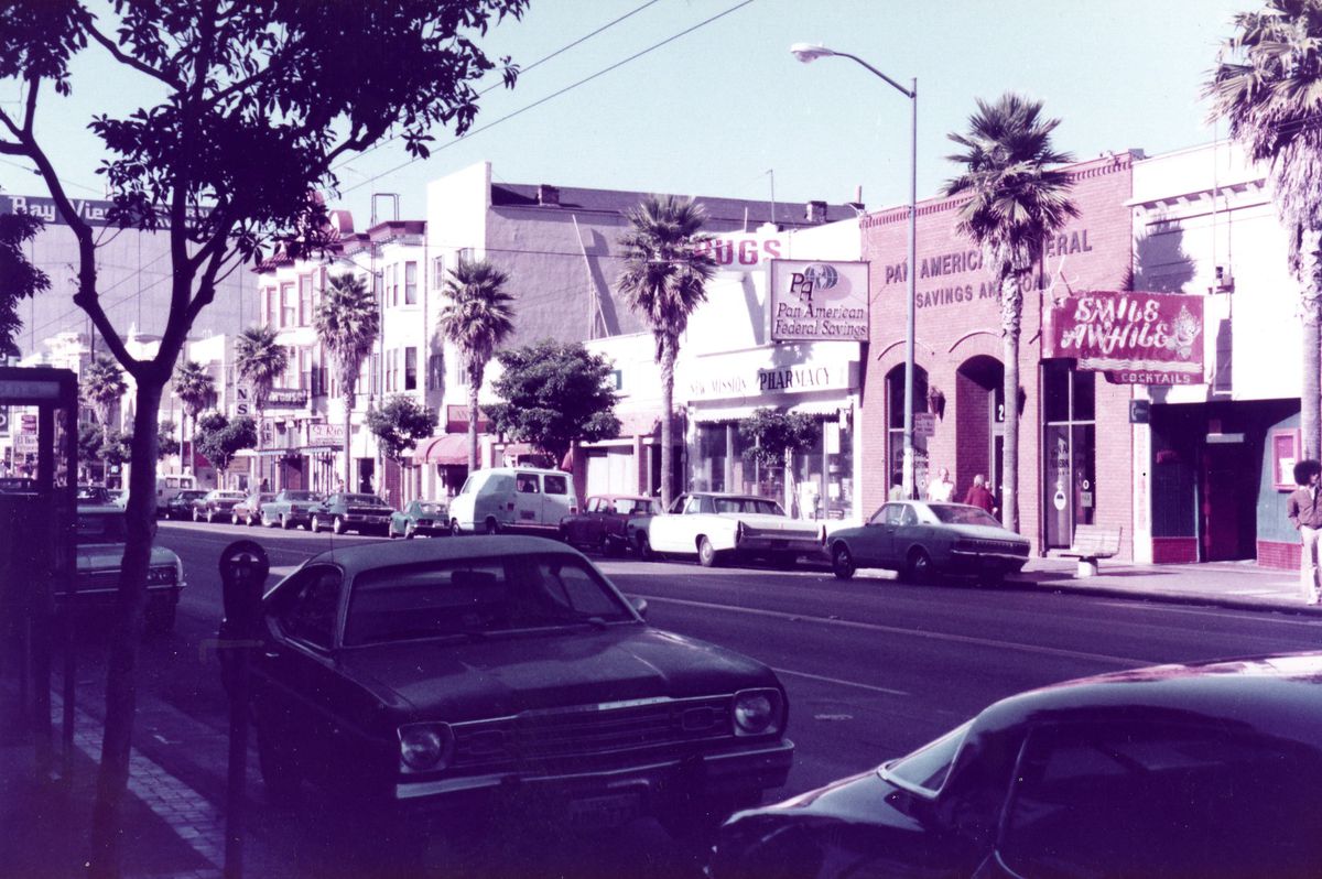 A 1978 photo of a street in San Francisco, California, showing palm trees, a drug store, and a bar.