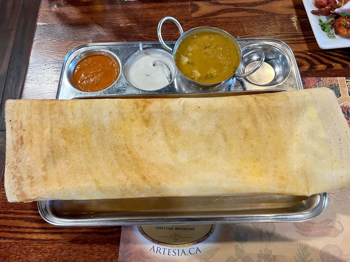 An egg dosa in a silver platter with two chutneys and sambar.