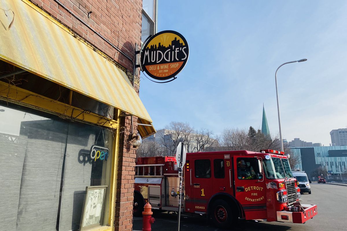 A red fire truck parked next to a stop sign at the corner of Porter and Brooklyn in Detroit. Yellow and white awning and sign that says Mudgie’s also pictured.