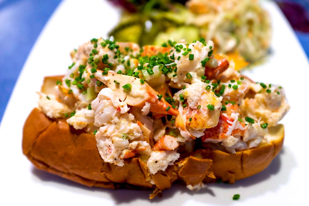A lobster roll sits atop a white plate, and is topped with shockingly green minced chives.