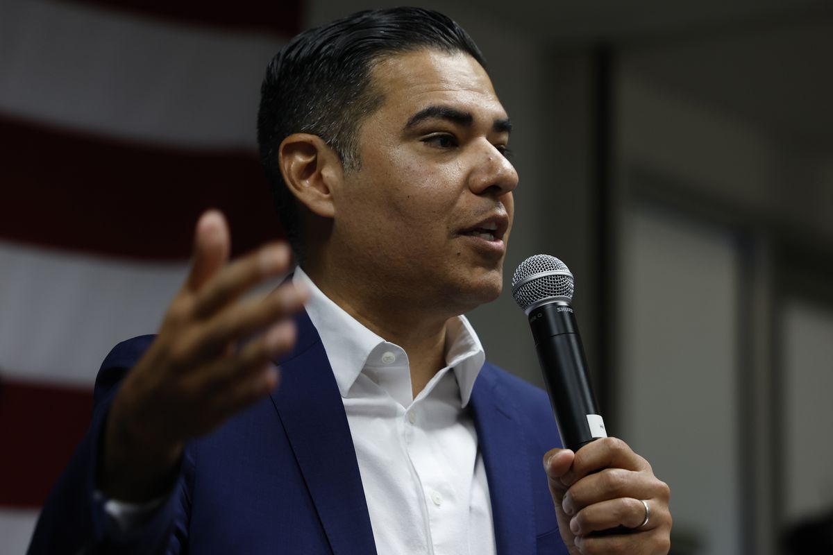 Rep. Robert Garcia, wearing a blue suit jacket and white shirt, gestures widely while speaking into a microphone.