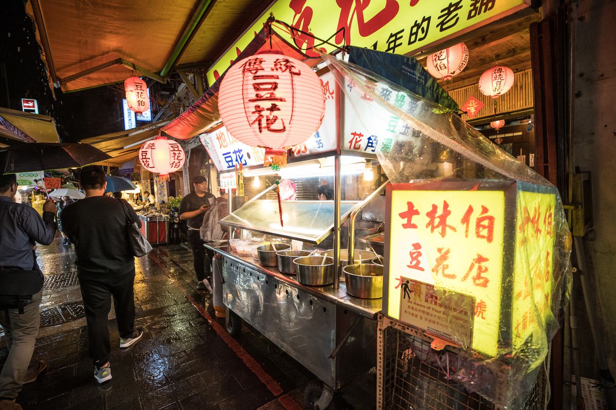 People wait outside a lit boba stall with hanging lanterns at the Shilin Night Market in Taipei, Taiwan.