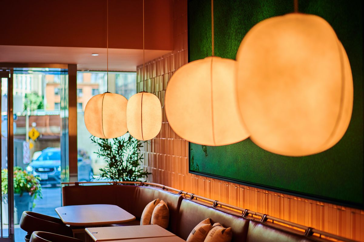 A dining room with hanging globe lights, wooden tables, and a green wall  on one side.