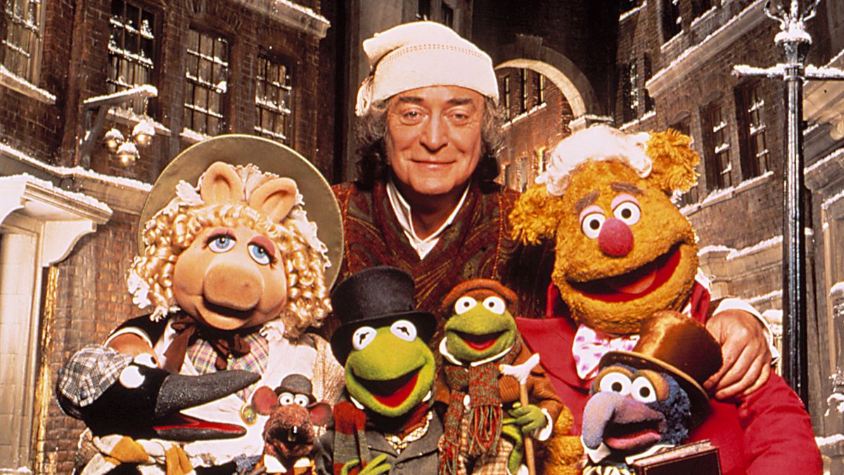 Miss Piggy, Michael Caine, Fozzie Bear, a penguin, Rizzo, Kermit, Robin, and Gonzo pose in their Muppet Christmas Carol costumes.