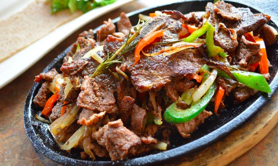 A black metal plate holds strips of cooked beef, onion, and green peppers