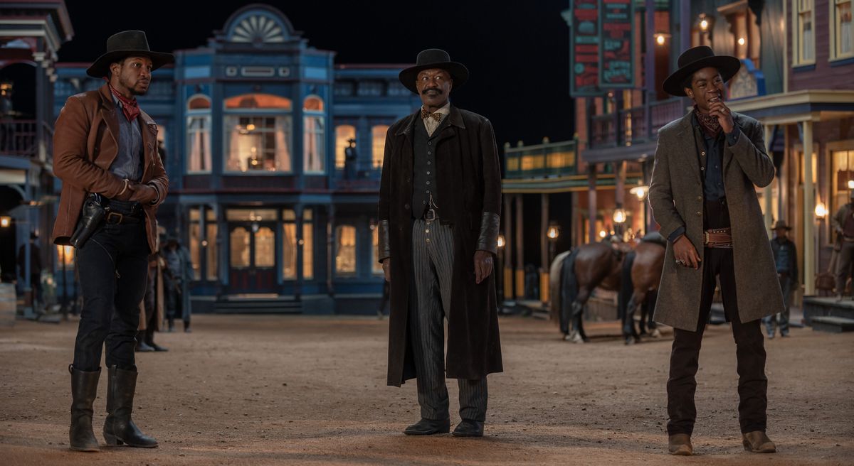 Jonathan Majors, Delroy Lindo, and RJ Cyler, in vintage Old West costumes, stand outside on a street at night in The Harder They Fall.