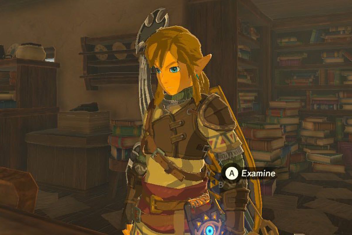 A screenshot of Link from the Legend of Zelda: The Breath of the Wild. He’s reading a book at the table and is surrounded by stacks and bookshelves full of books.