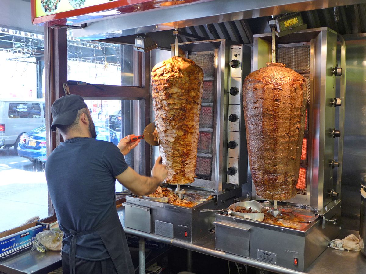 Two twirling cylinders of meat with a man standing in front, his back to us, wielding a knife.