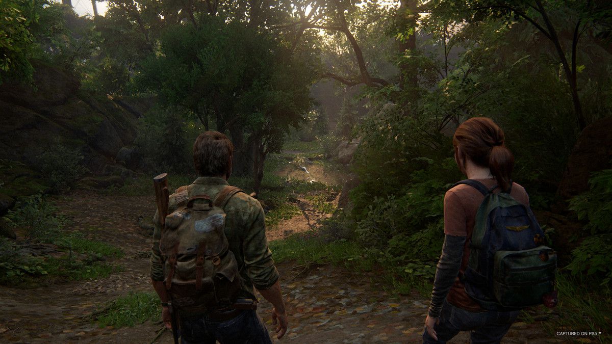 Joel and Ellie walk through a heavily forested area in The Last of Us Part I