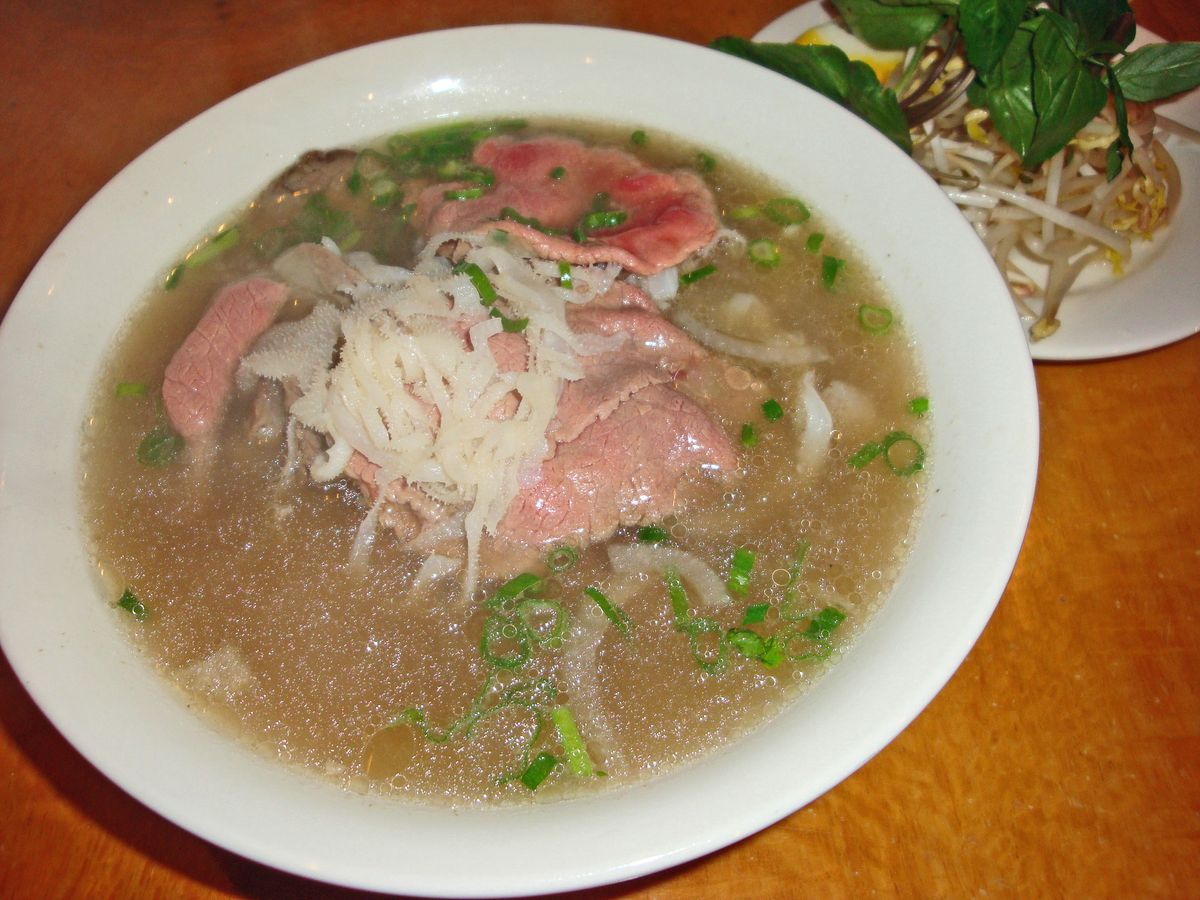 A bowl of pho with sliced raw steak floating on top.