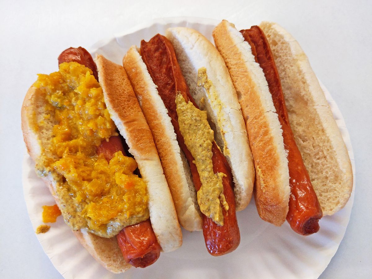 Three hot dogs in buns, with mustardy relish and mustard on two of them.