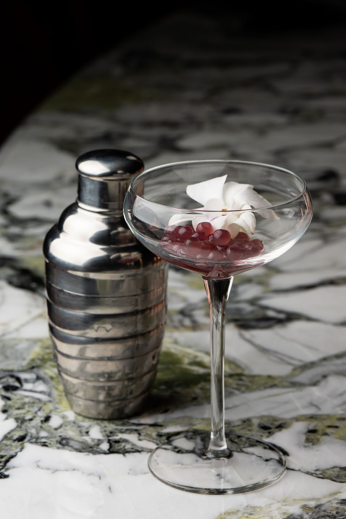 A cocktail at the ready with pomegranate, on a marble table.