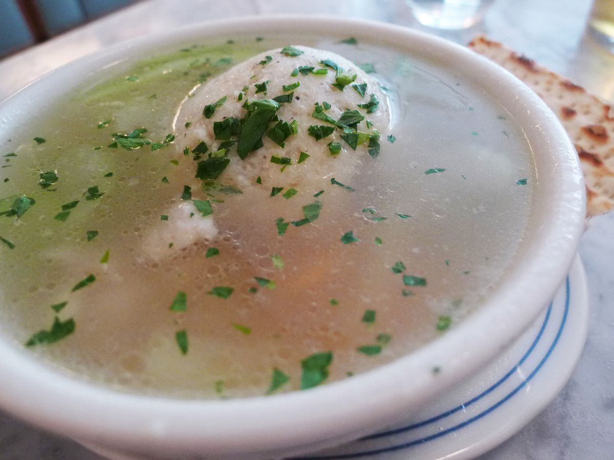 A bowl of parsley strew soup with a big matzo ball sticking up.