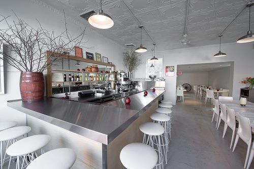 The sleek white interior of Casa Enrique and its metallic bar lined with white stools.