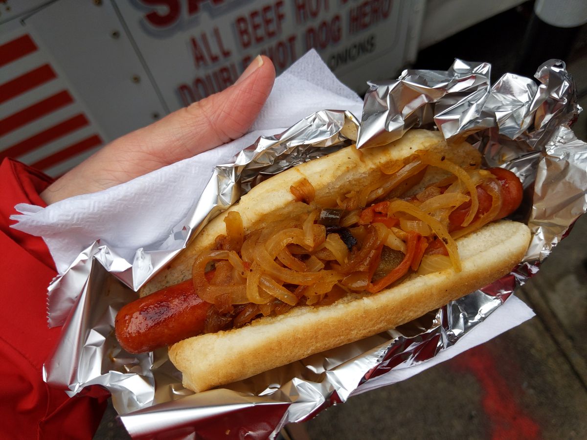 A beautiful hot dog held in a hand and cradled in aluminum foil.