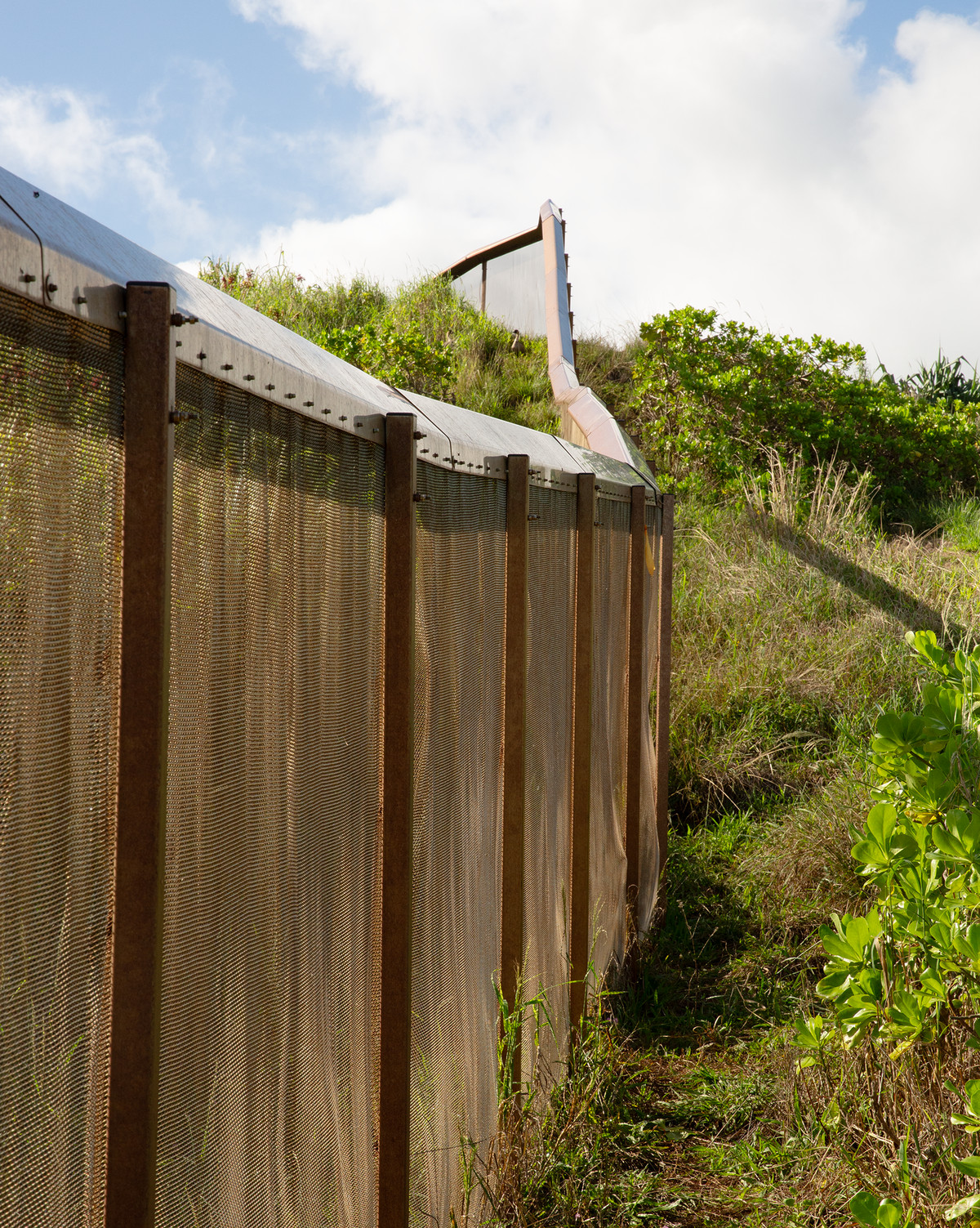 A fence whose posts are connected by a mesh-like netting bisects a grassy hill.