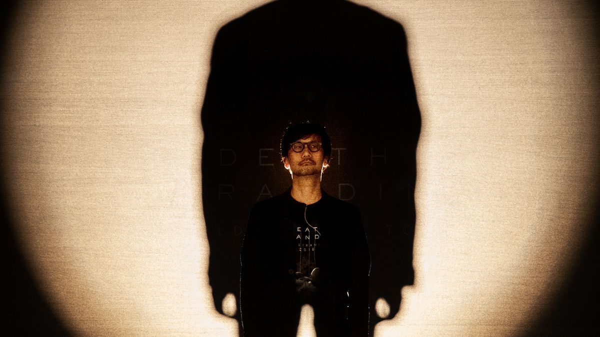 Hideo Kojima standing on stage casting a looming shadow