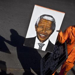 FILE - In this  Thursday, June 27, 2013, file photo, an arriving well wisher carries a portrait of Nelson Mandela as he walks down the street outside the entrance to the Mediclinic Heart Hospital where former South African President Nelson Mandela is being treated in Pretoria, South Africa. Makaziwe Mandela, daughter of Nelson Mandela, said Thursday he is in very critical condition but is still opening his eyes and reacting to touch at the South African hospital where he is being treated. 