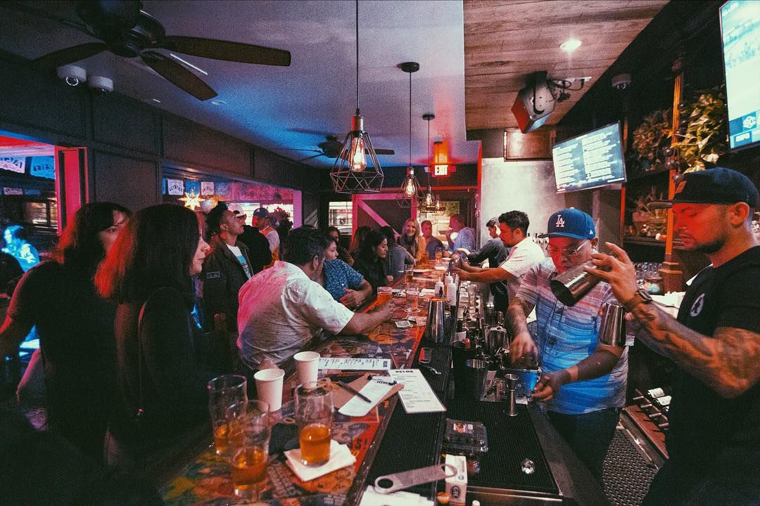A packed bar with neon vibes as bartenders reach for cash.