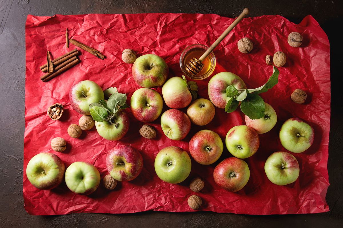 Ripe organic gardening green red apples with leaves. nuts. cinnamon and jar of honey on red bright crumpled paper over dark texture background. Flat lay. space. Autumn harvest.