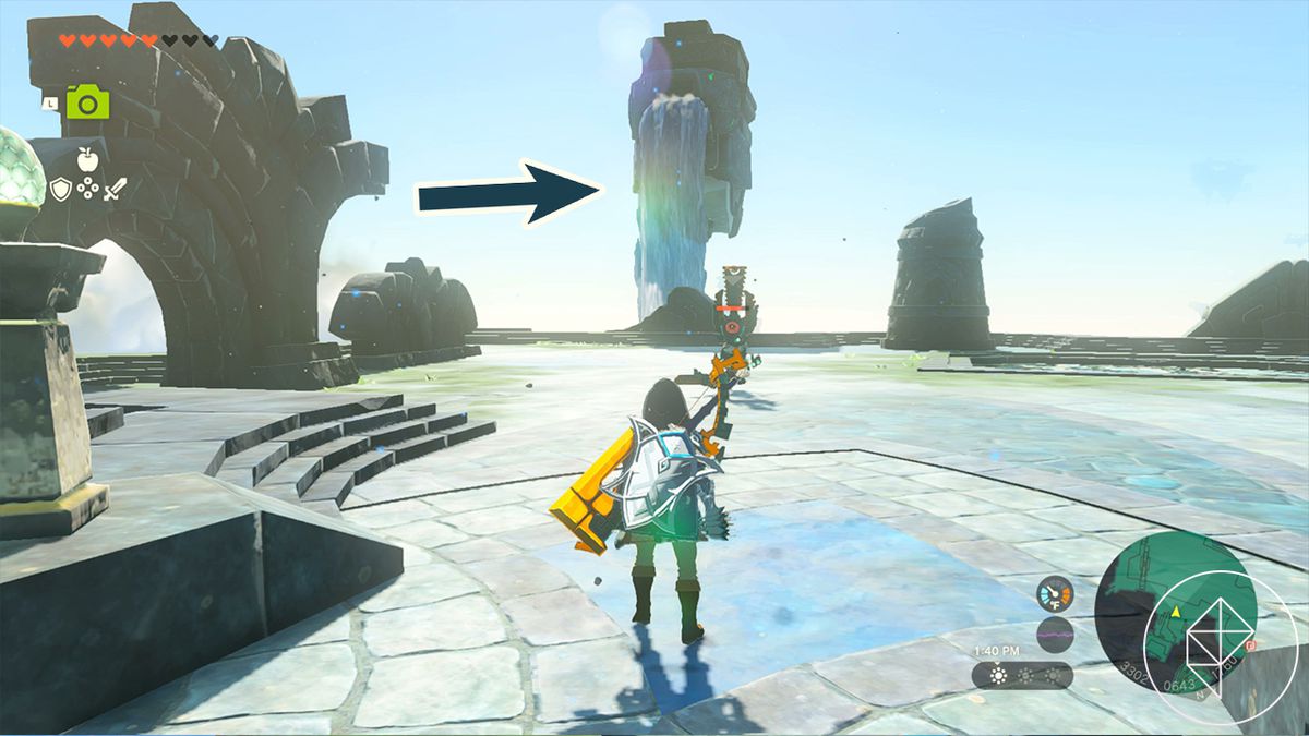 Link stands in a decorative stone landing, and across from him, a stone pillar with a waterfall blocked by mud. A superimposed arrow points to the waterfall, indicating that’s what Link must clean off.
