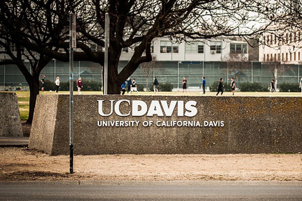 The UC Davis logo with a soccer game and bike riders in the background. University of California at Davis. Davis, California. Taken February 2, 2015.