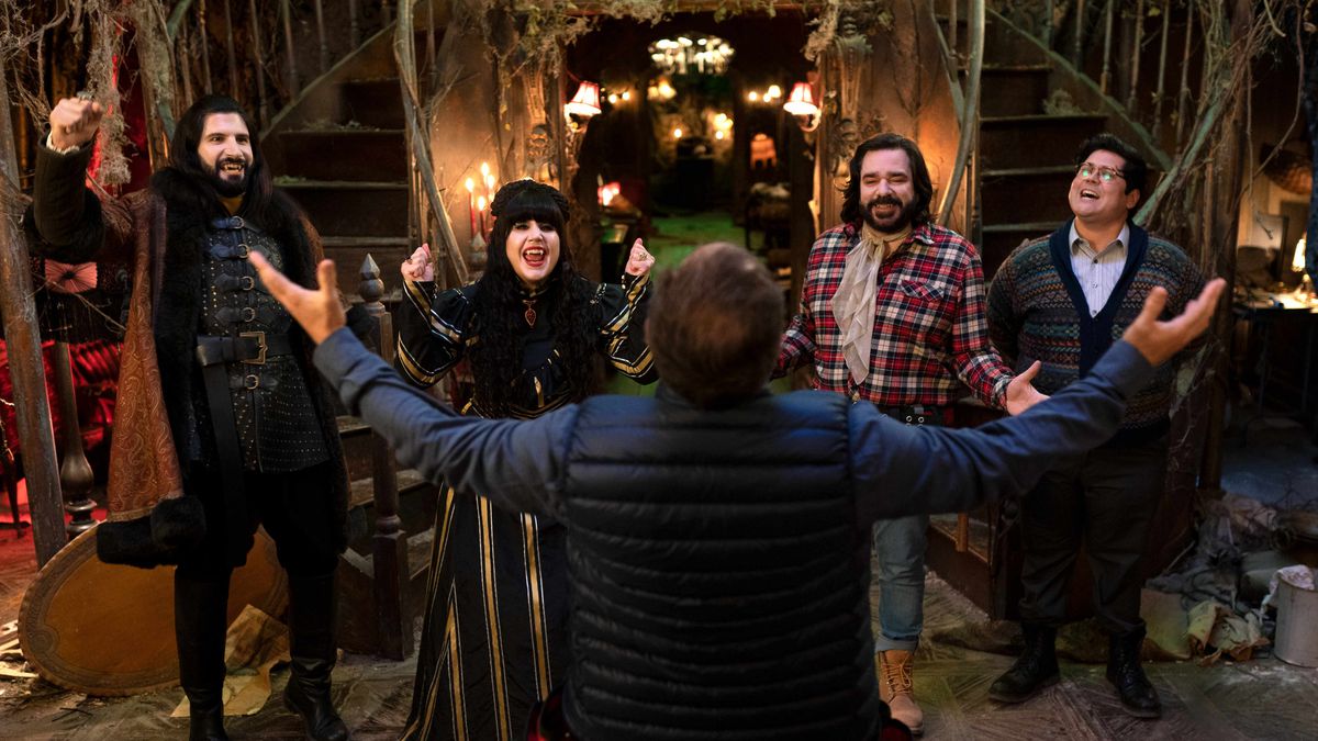 Nandor (Kayvan Novak), Nadja (Natasia Demetriou), Laszlo (Matt Berry), and Guillermo (Harvey Guillén) cheer along with the host of “Go Flip Yourself” in a still from “What We Do in the Shadows”