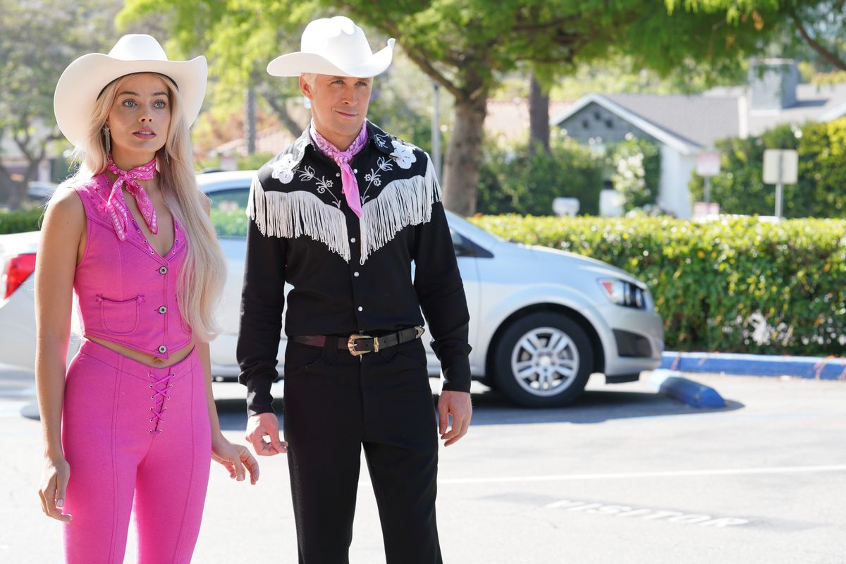 Margot Robbie as Barbie, wearing a pink cowgirl outfit, standing next to Ken, who wears a matching black cowboy fit. 