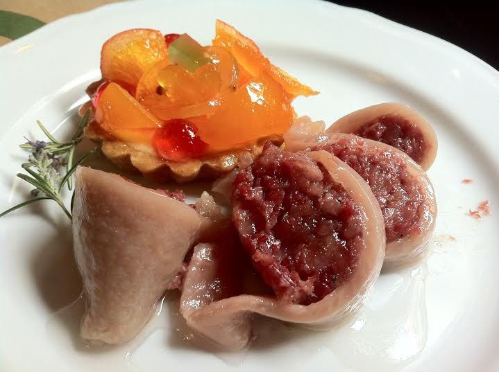 A meaty offal dish on a plate with sliced tomatoes