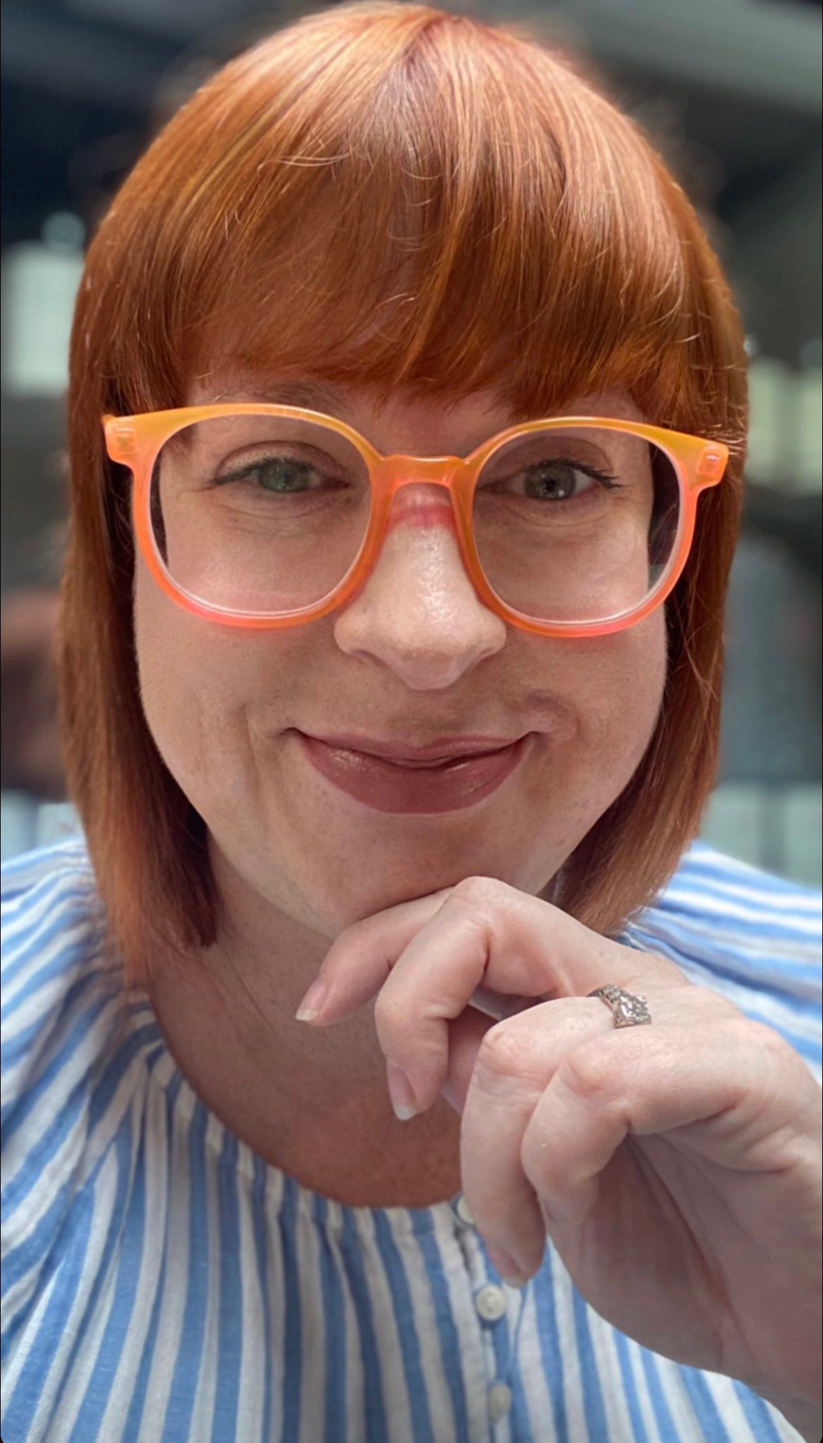 Heather Lesher smiles at the camera with cropped red hair and orange glasses frames.