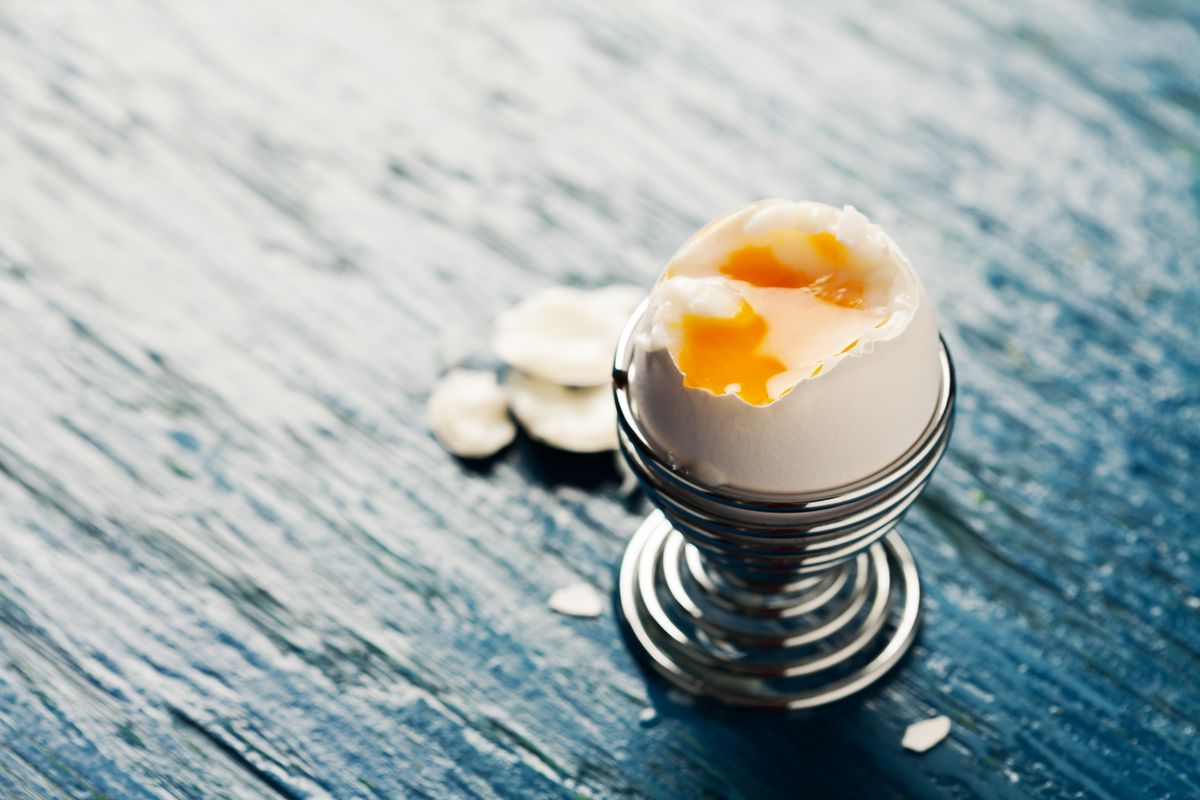 A soft-boiled egg sitting in an egg cup with its top shell open.