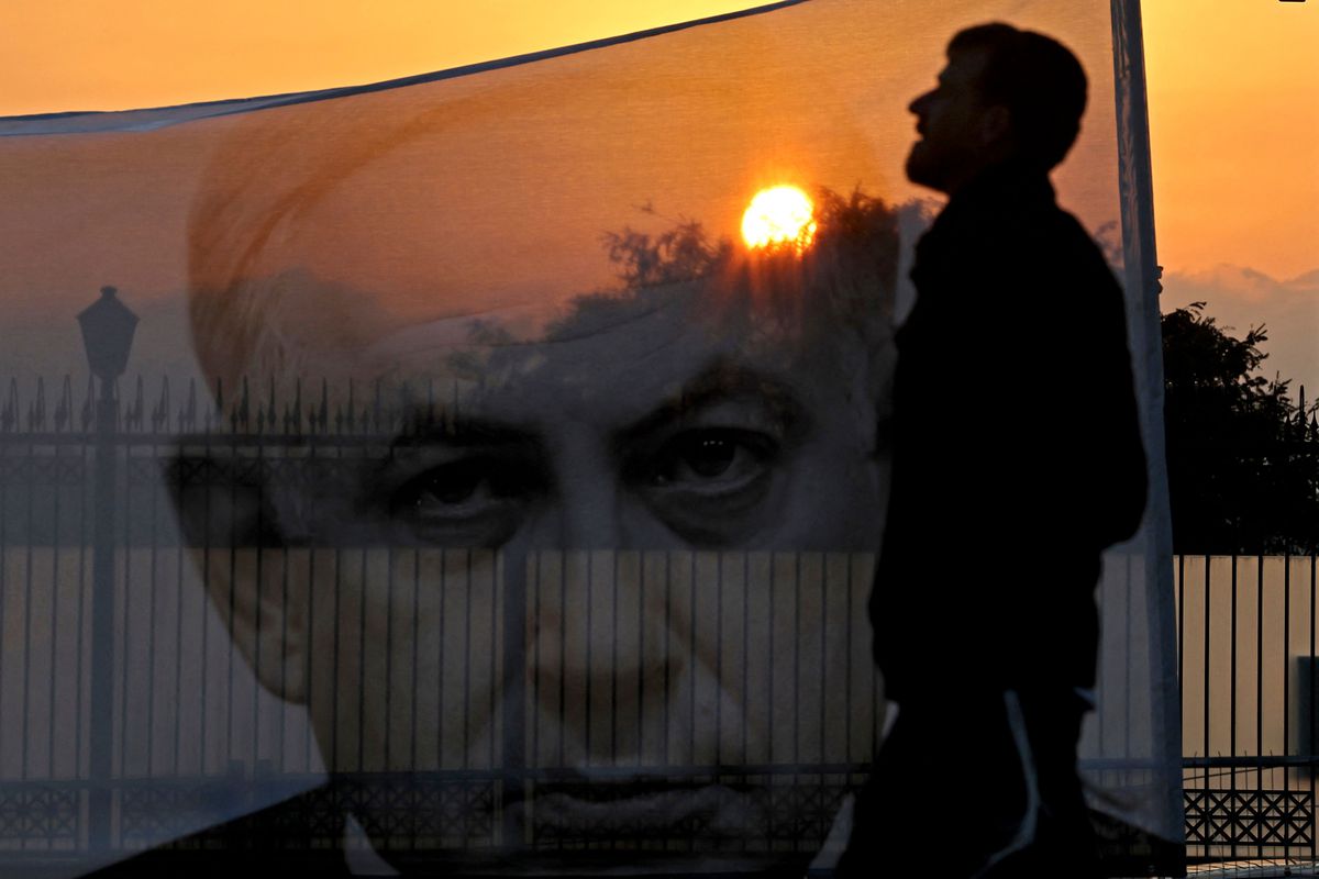 A man is seen in silhouette against a banner featuring Netanyahu’s face, with the sunset in the background.
