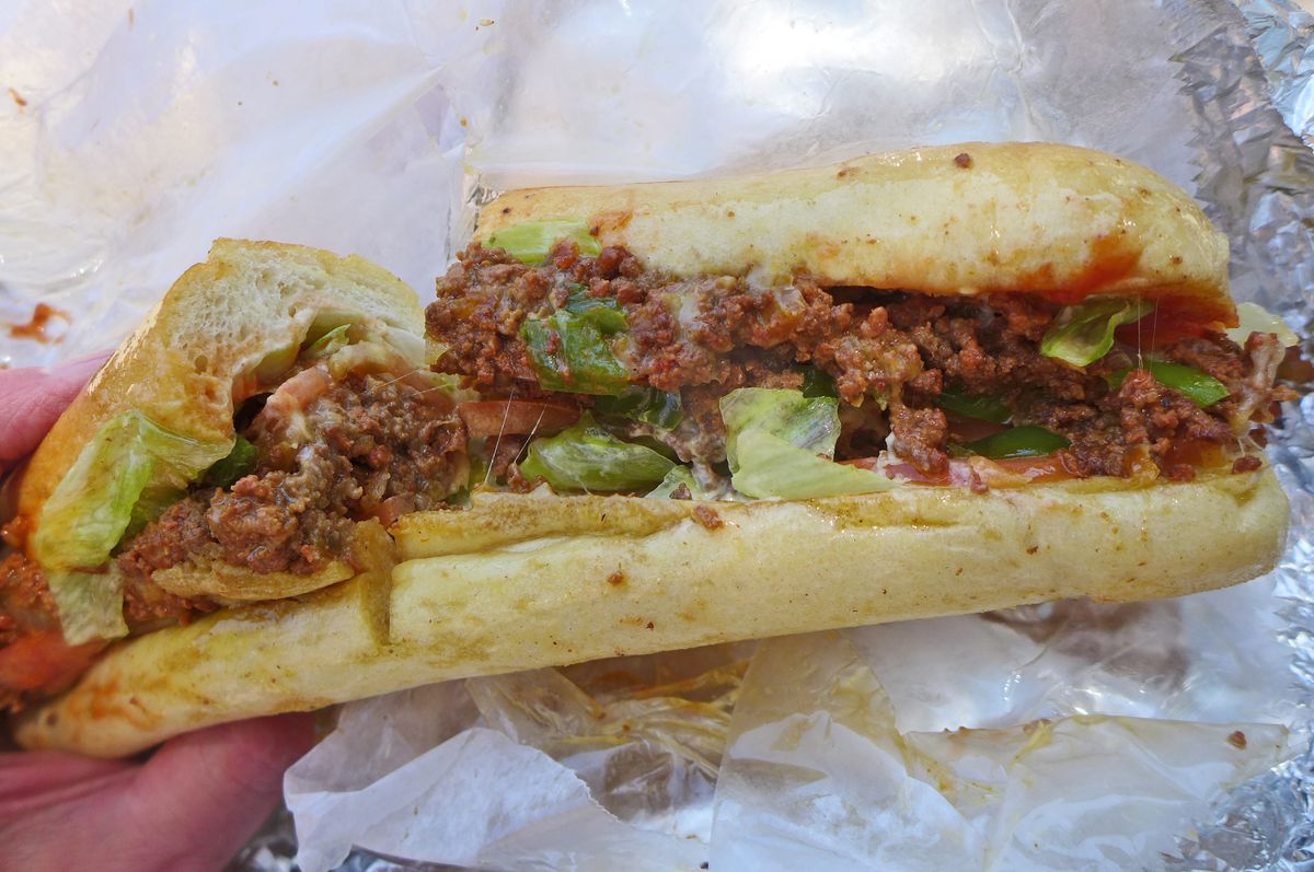 A long damp sandwich on a baguette with ground beef prominent.