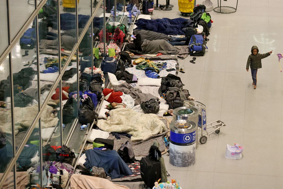 Blankets and suitcases cover the floor as migrant families are left to sleep at Boston’s international airport.