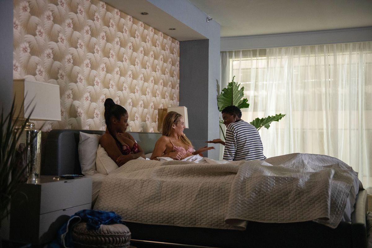 Janicza Bravo sits on a bed beside Taylour Paige and Riley Keough during the filming of Zola.