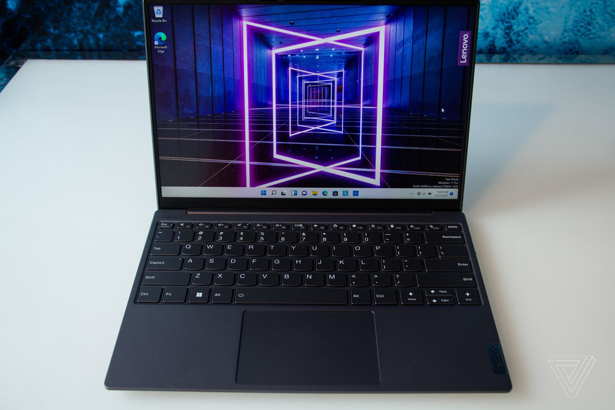 The Lenovo Slim 7i Carbon on a white table seen from above. The screen displays a dark hallway with neon pink outlines.