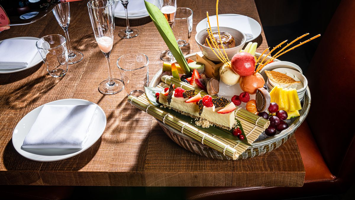 A fancy desserts platter with ice cream and cheesecake on a wood table near a pour of Champagne
