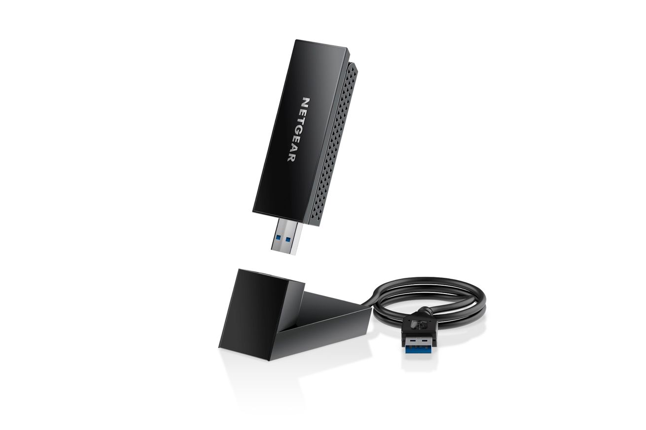 A black USB thumb drive-looking device with the Netgear logo is floating above a small matching docking station as if it’s about to be plugged in. There’s a cable that is coming from the rear of the dock and is coiled and terminating with a blue USB-A male connector.