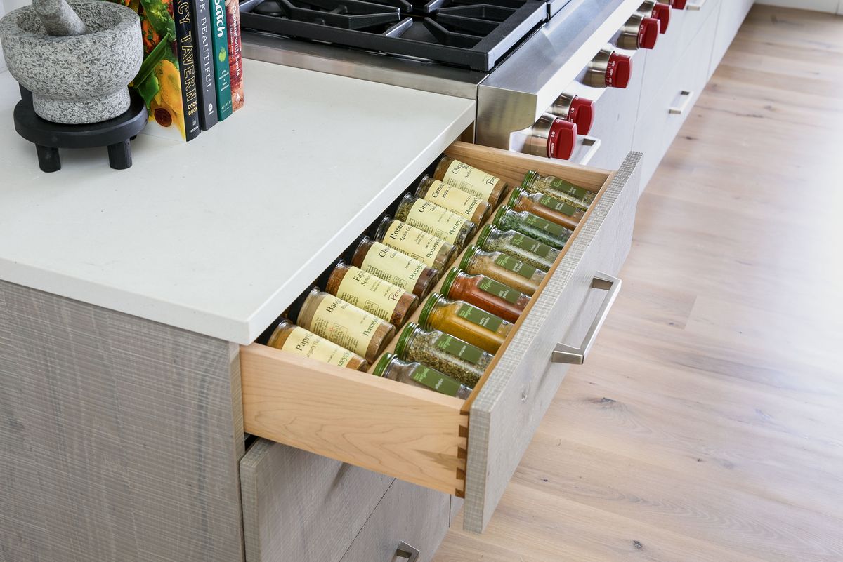 A newly renovated kitchen with a drawer open, filled with spices. A mortar and pestle and cookbooks sit on the counter.