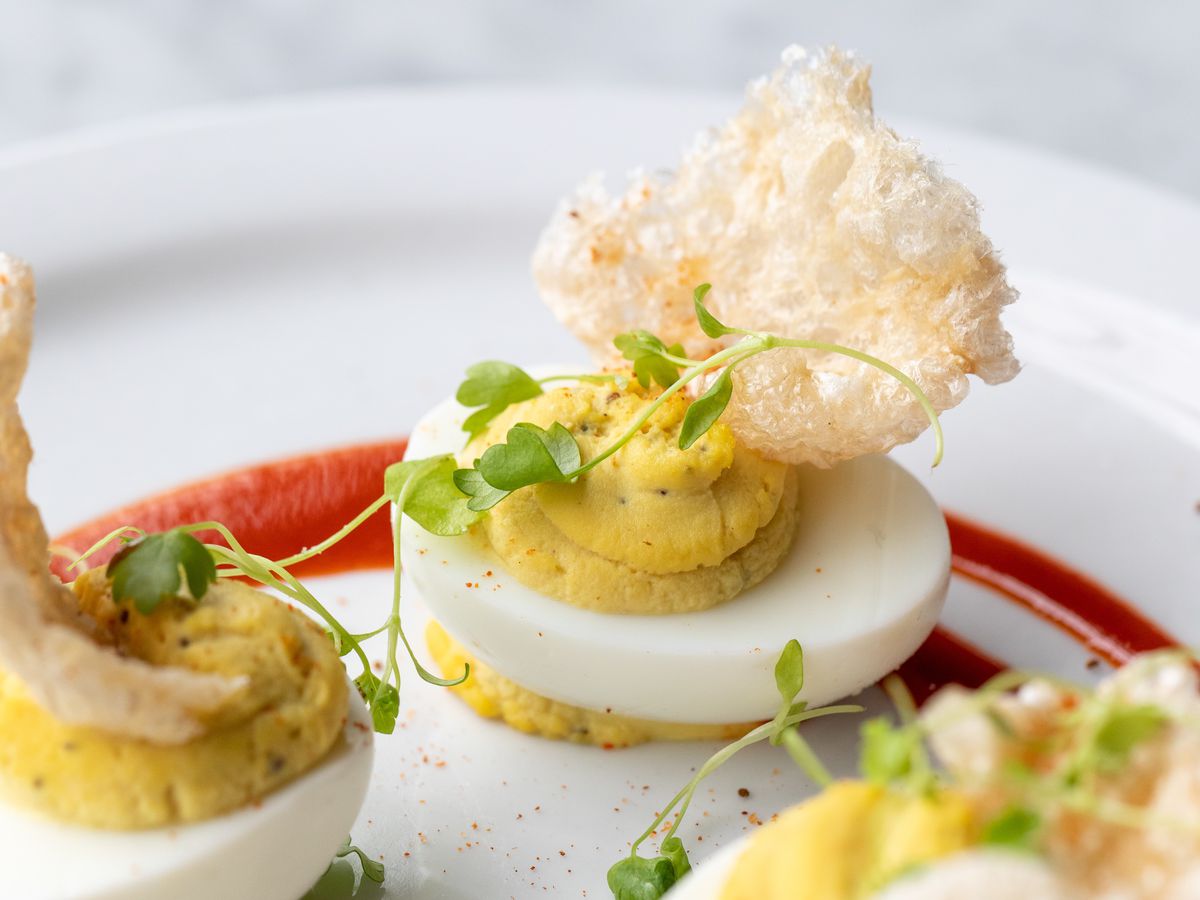 A deviled egg on a plate with pea shoots and pork rinds.