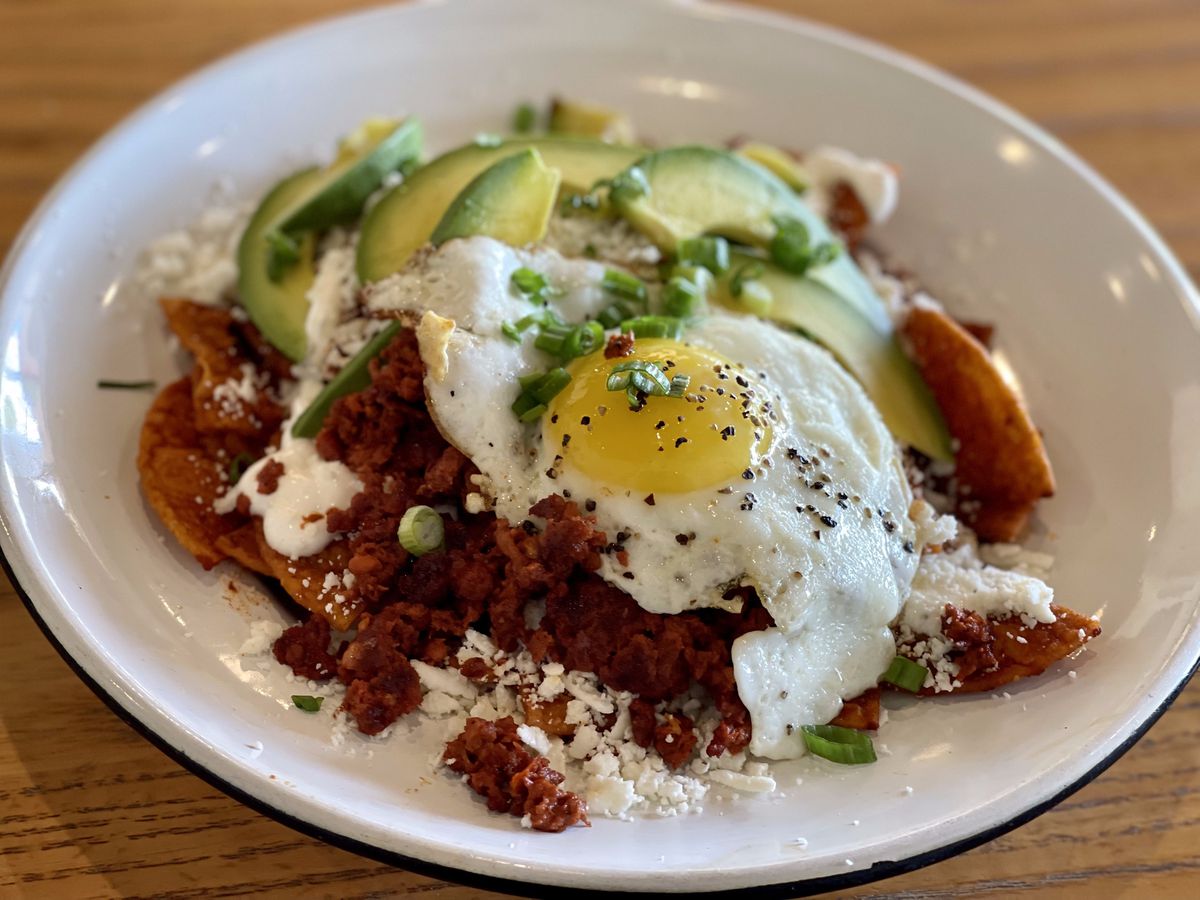 A bowl of chilaquiles topped with a fried egg, avocado, and green onion at Cochinita &amp; Co.