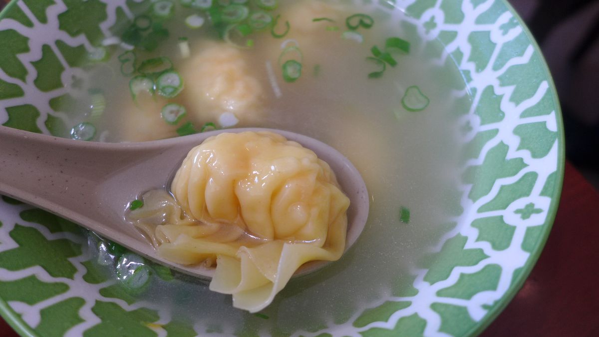 A spoon holds a dumpling above a green bowl.